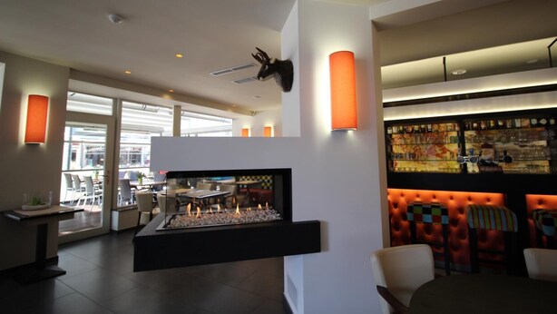 A modern interior with a fireplace, seating area, and a bar with a colorful mural. - Hotel La Terrasse (De Panne)