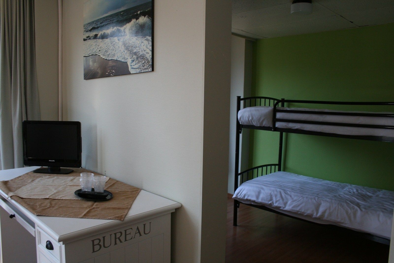 A room with a bunk bed, a desk with a computer, and a painting of a beach scene.