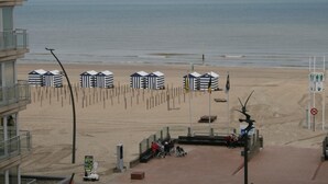 A beach with striped beach huts, a wheelchair ramp, and a no swimming sign. - Hotel La Terrasse (De Panne)