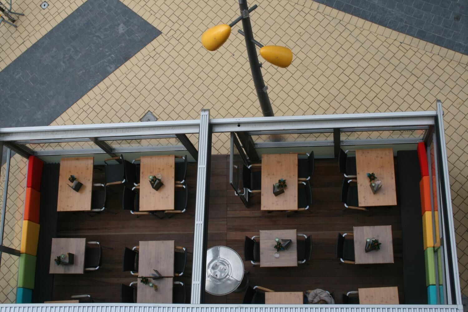An outdoor seating area with multiple tables and chairs, a metal railing, and a yellow hanging light fixture.