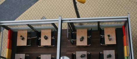 An outdoor seating area with multiple tables and chairs, a metal railing, and a yellow hanging light fixture.