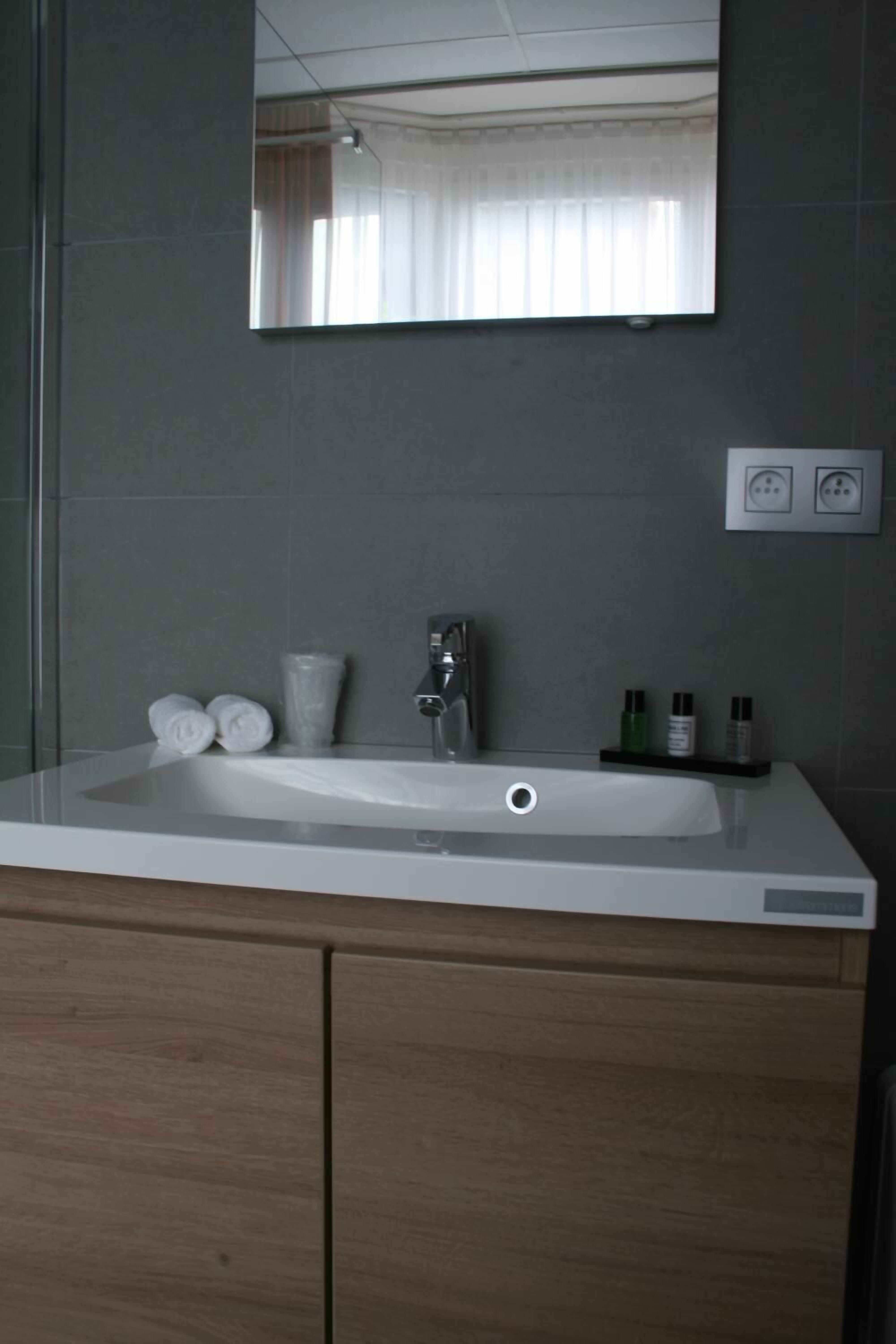 A bathroom with a white sink, a mirror, and a wooden cabinet. There are towels and toiletries on the sink.