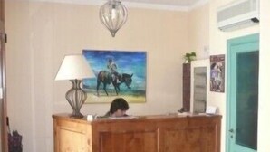 A reception desk with a lamp, a painting of a horse, and a teal door. - Albergo La Fontanella (Noto)