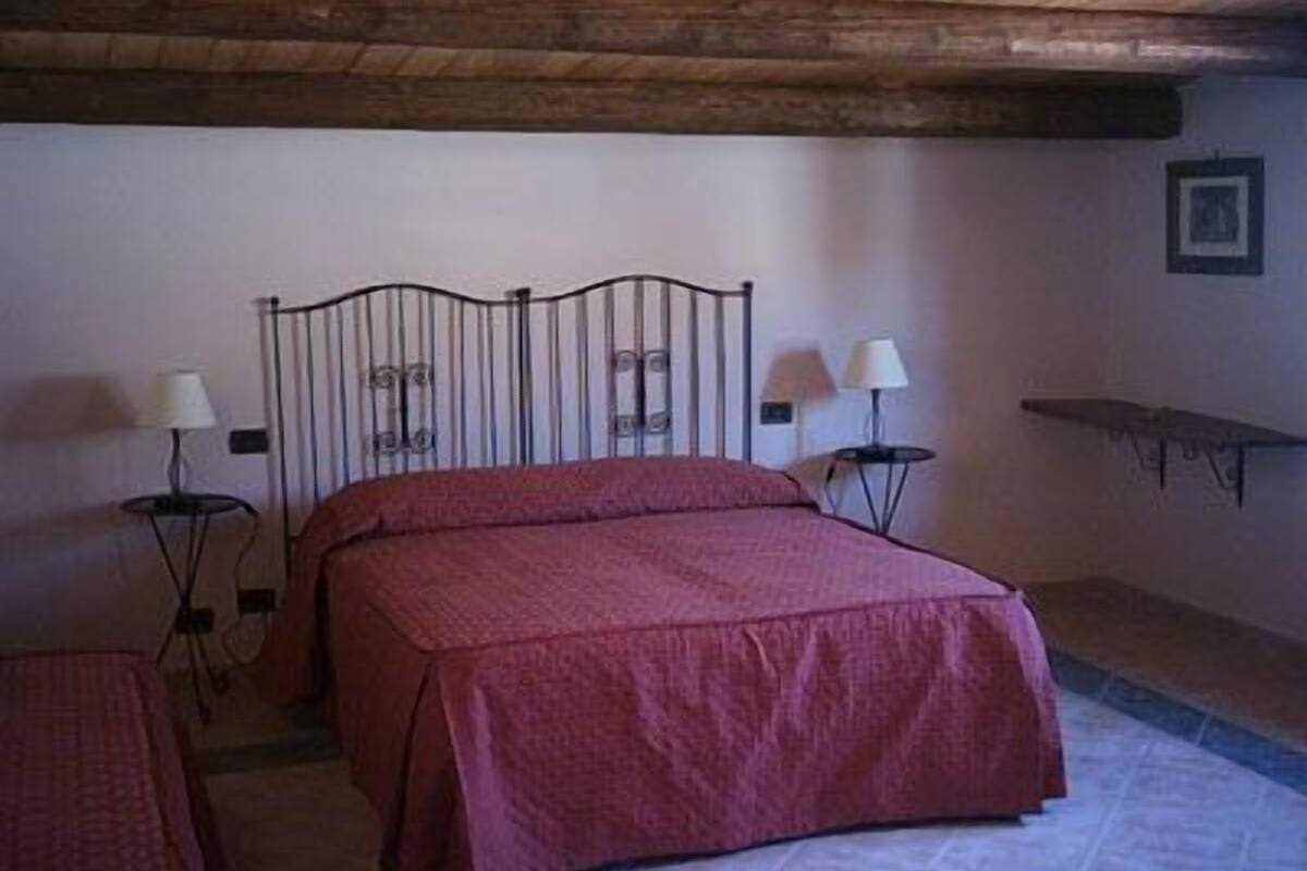 Un dormitorio con una cama, dos mesitas de noche con lámparas, techo de madera y una pequeña estantería.