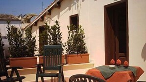 An outdoor patio with a table and chairs, potted plants, and a door. - Albergo La Fontanella (Noto)