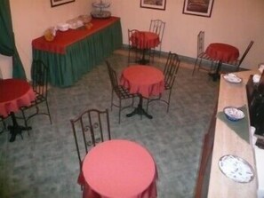 A dining area with round tables and chairs, a buffet table with food, and framed pictures on the wall. - Albergo La Fontanella (Noto)