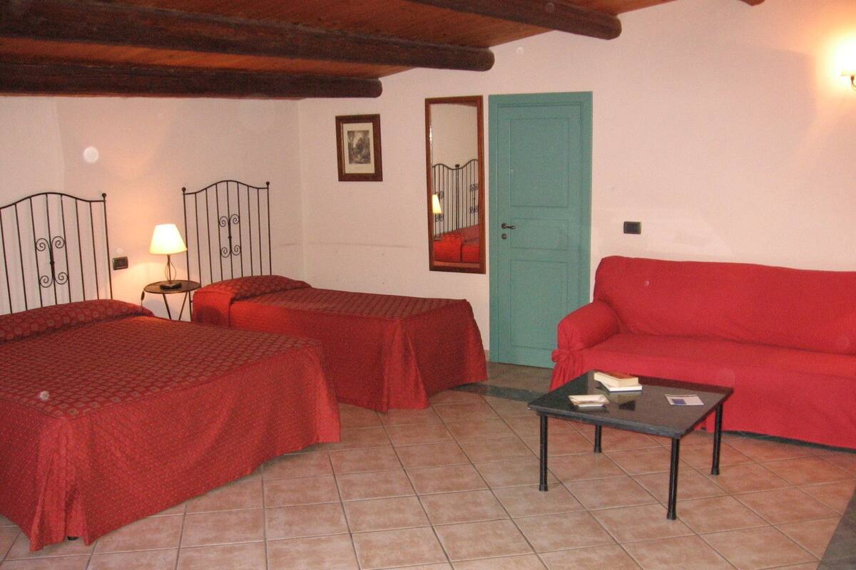 Una habitación con dos camas, un sofá rojo, una mesita y una puerta.