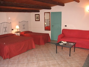 A room with two beds, a red sofa, a small table, and a door. - Albergo La Fontanella (Noto)