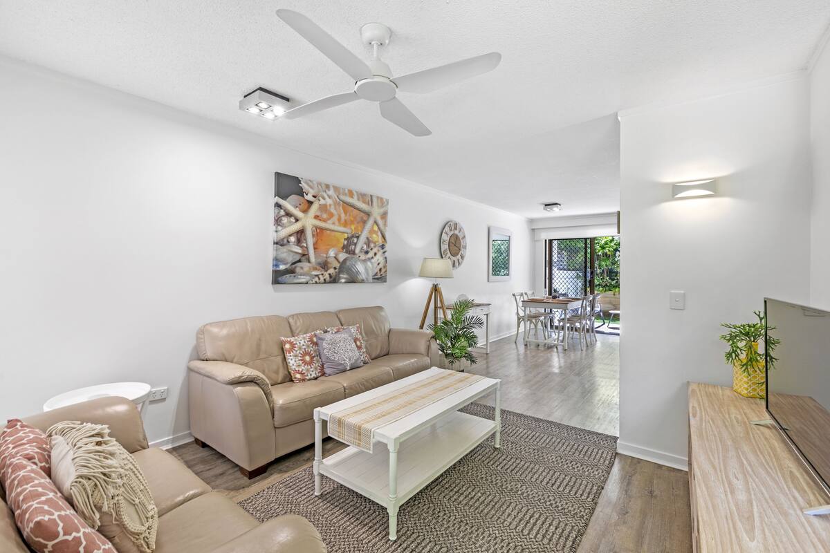 A modern living room with a beige sofa, a white coffee table, and a ceiling fan.
