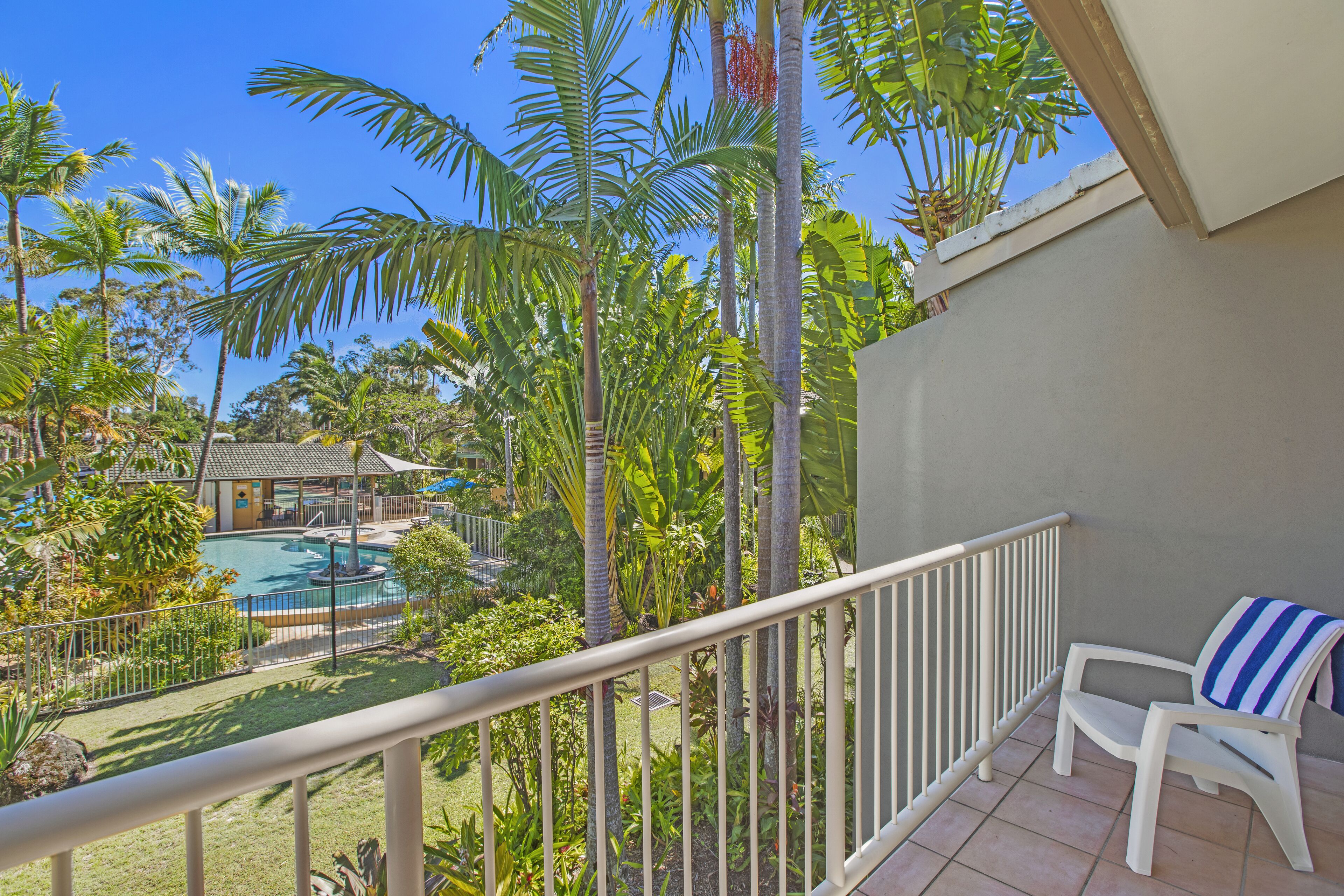 A balcony with a view of a swimming pool surrounded by tropical vegetation.