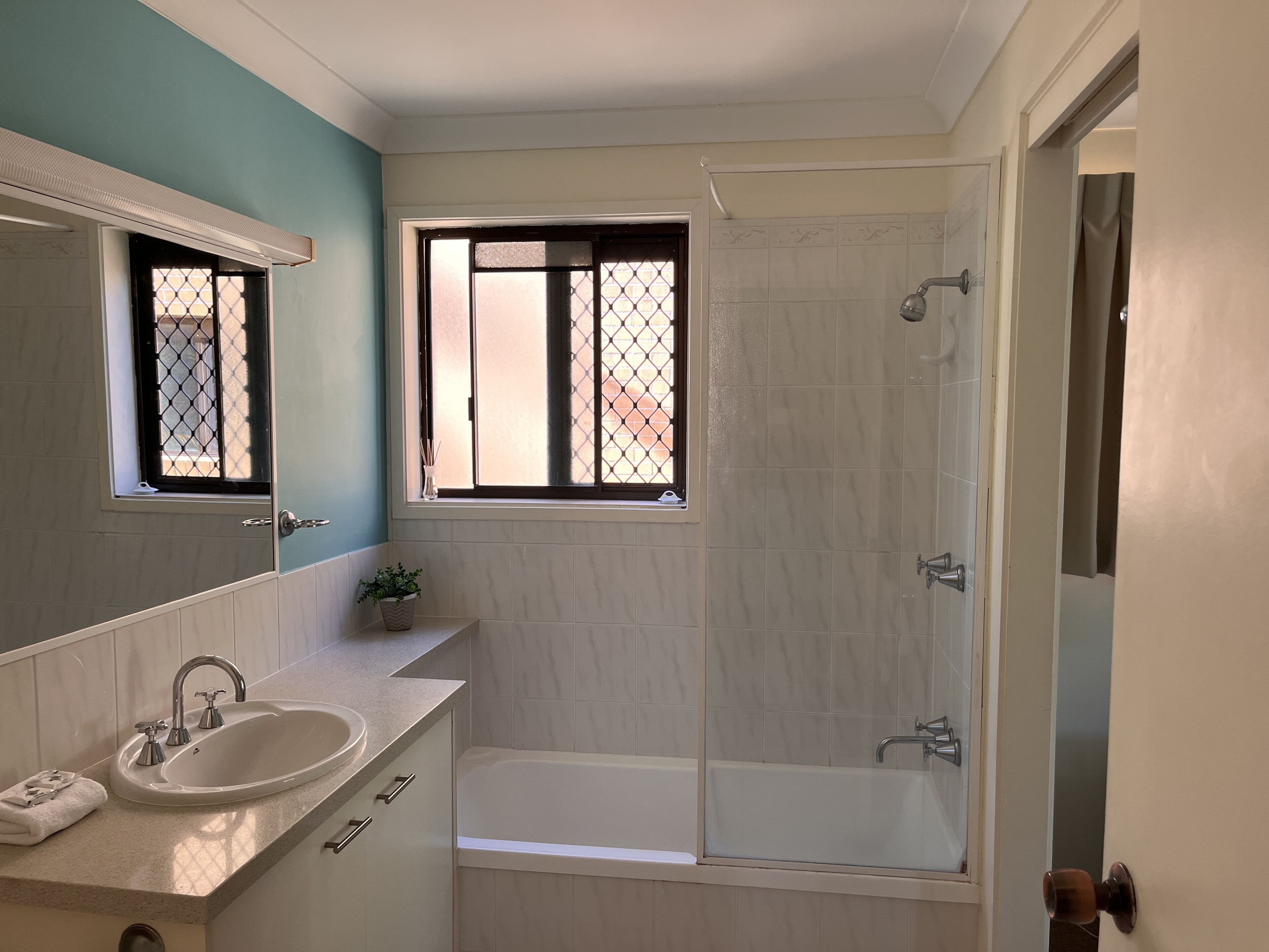 A bathroom with a sink, mirror, window, and bathtub.