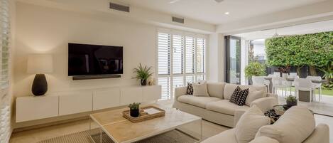Una sala de estar moderna con sofá, mesa de centro, televisor y vistas al exterior.