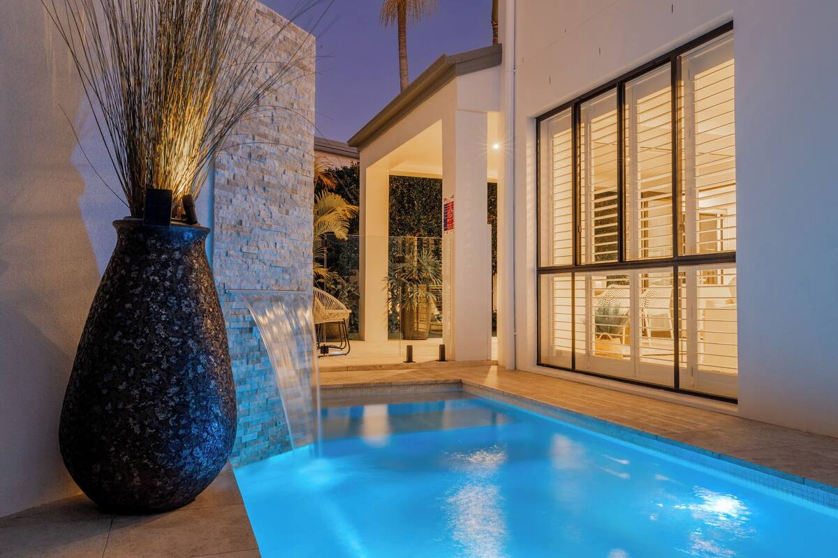 A modern pool area with a clear blue pool, a large decorative vase, and a well-lit interior space.