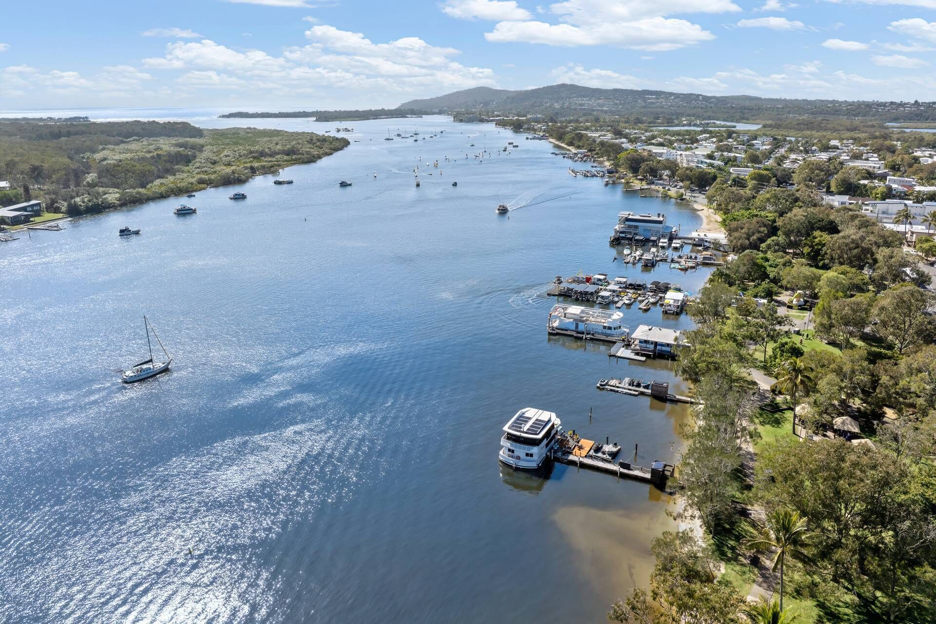 A marina with multiple boats docked, a large yacht, and a residential area with houses and greenery along the waterfront.