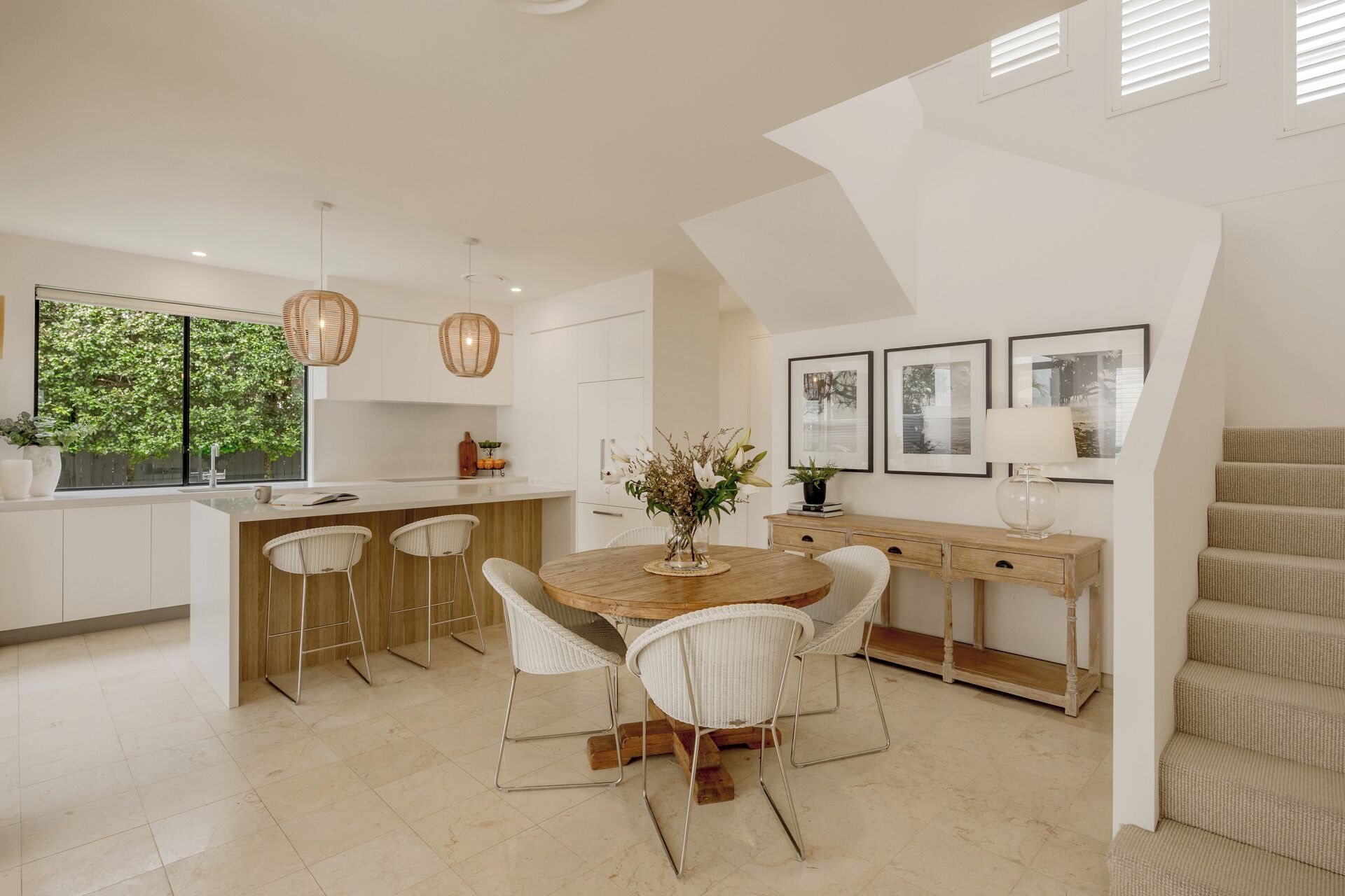 A modern kitchen with a central island, white cabinetry, and a dining area with wicker chairs.