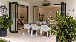 Un espacio de sala-comedor abierto con una mesa de comedor, sillas de mimbre blanco y plantas en macetas.