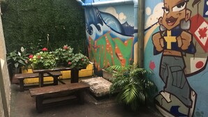 A small outdoor area with a green wall, a mural, a wooden bench, and potted plants. - Sydney City Hostel (Haymarket)