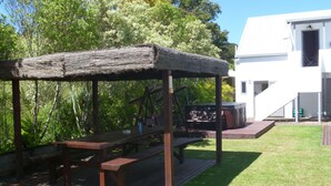 Un espacio al aire libre con asientos de madera, bancos y una mesa, un jacuzzi y un edificio blanco al fondo.