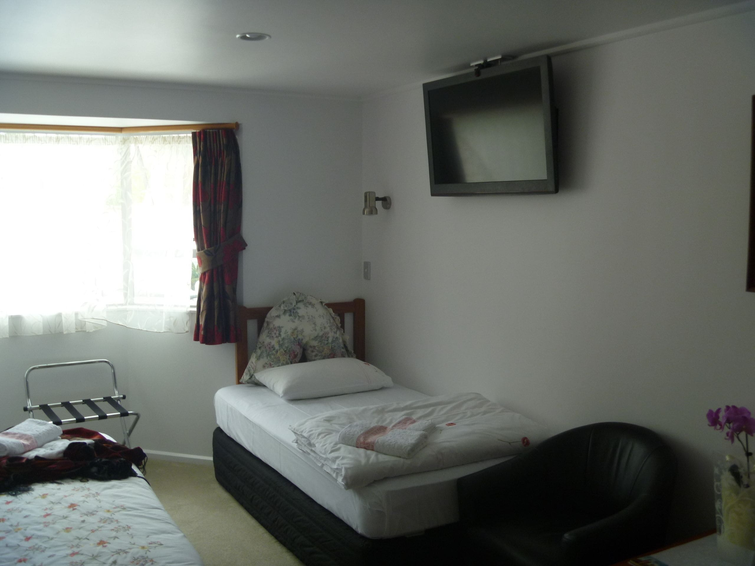 A bedroom with a bed, a chair, a small table, and a window with curtains.