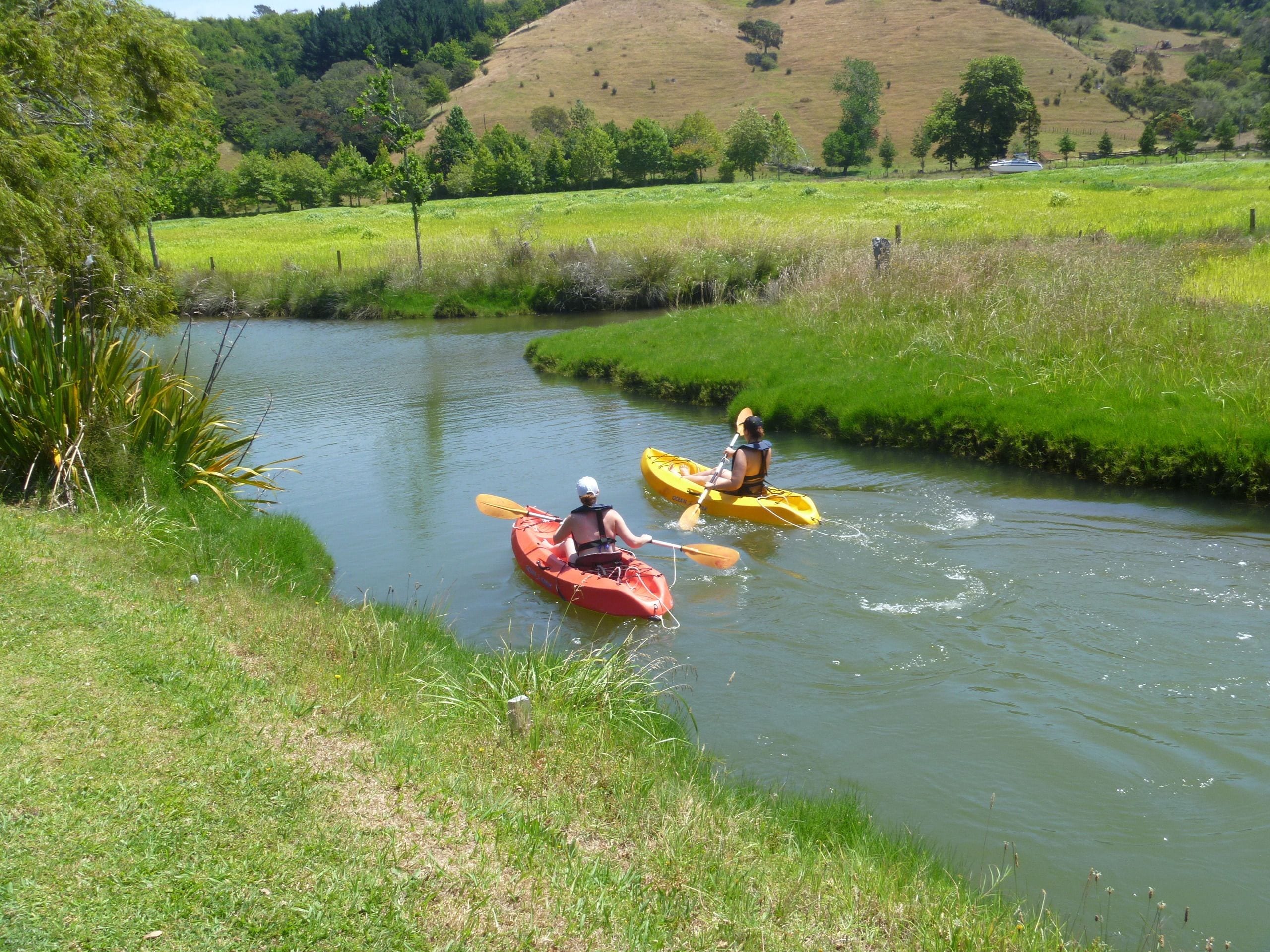 Two people kayaking on a calm river surrounded by lush greenery and hills.