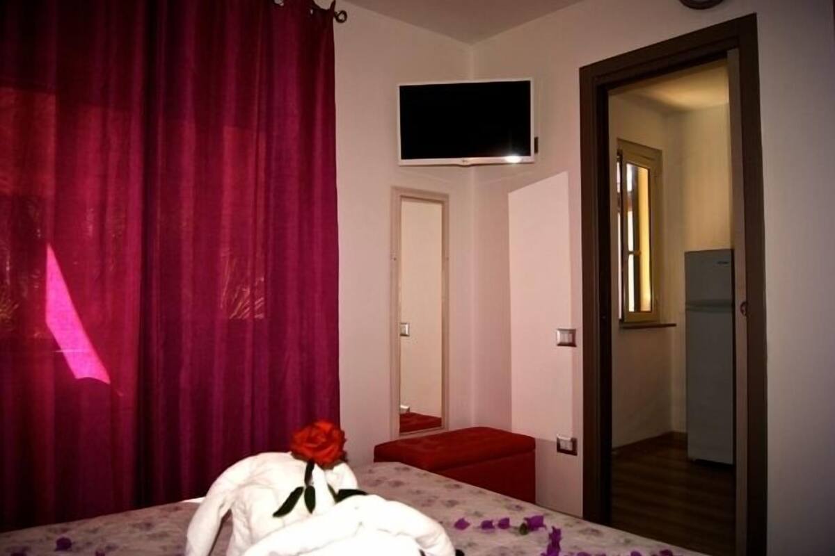 Ein Schlafzimmer mit einem Bett, einem an der Wand montierten Fernseher und einer Tür zu einem weiteren Raum.