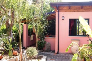 A pink building with a wooden pergola, potted plants, and a stone pathway. - Park Oasi Residence (Zambrone)