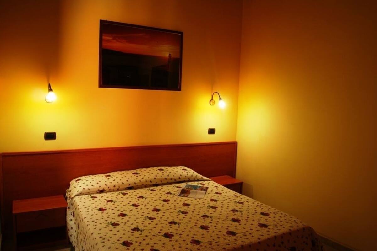 Ein Zimmer mit einem Bett, zwei Nachttischlampen und einem gerahmten Bild an der Wand.