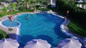 A swimming pool with a curved edge, surrounded by greenery and umbrellas. - Park Oasi Residence (Zambrone)