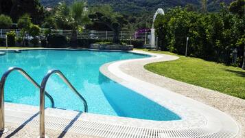 A swimming pool with a curved edge, surrounded by a pebble-lined deck and a grassy area.