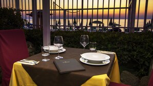 A table set for dining with a view of the sunset and a bridge in the background. - Park Oasi Residence (Zambrone)