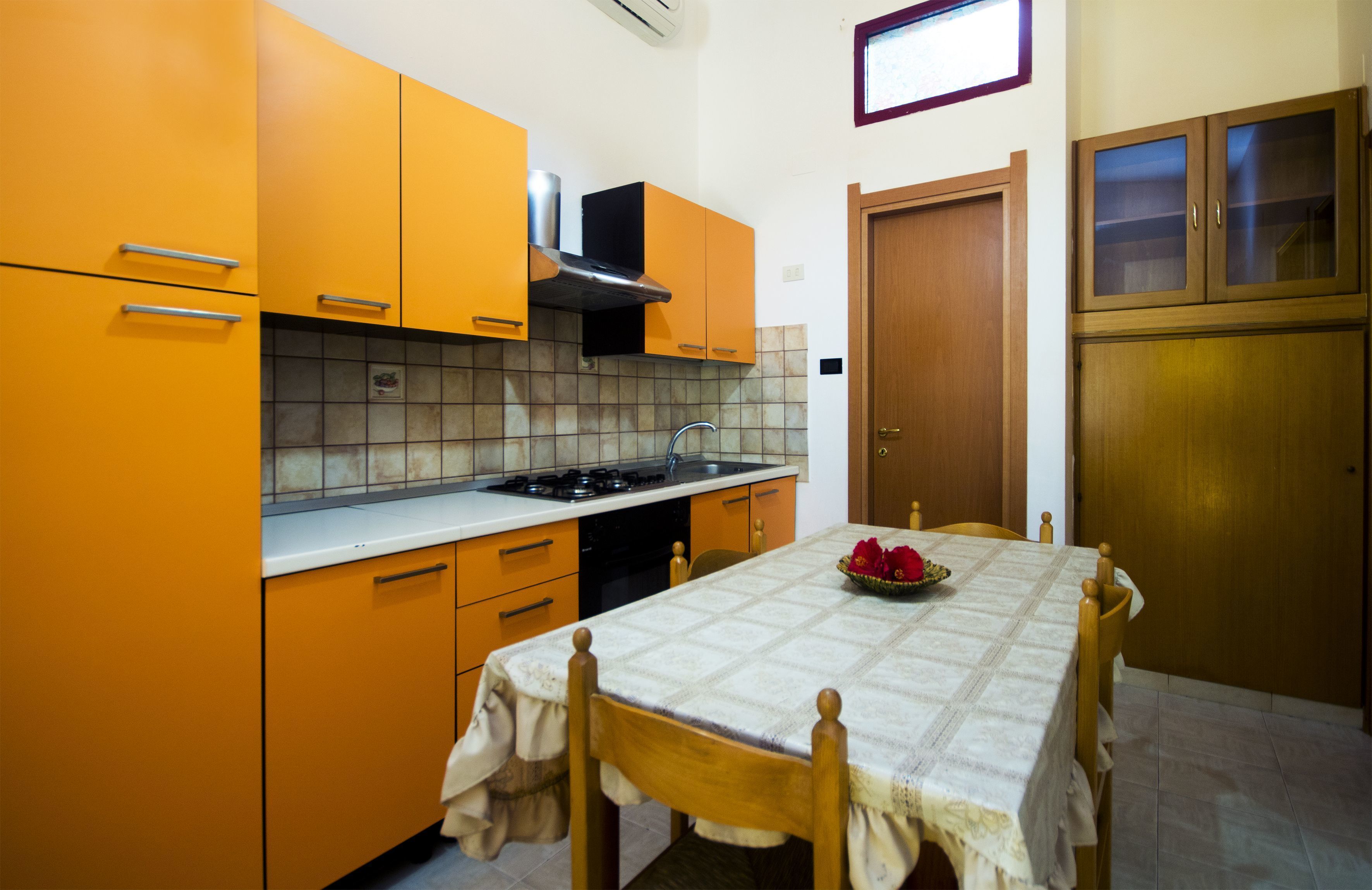 Una cocina con armarios color naranja, una estufa y una mesa de comedor con un centro de mesa floral.