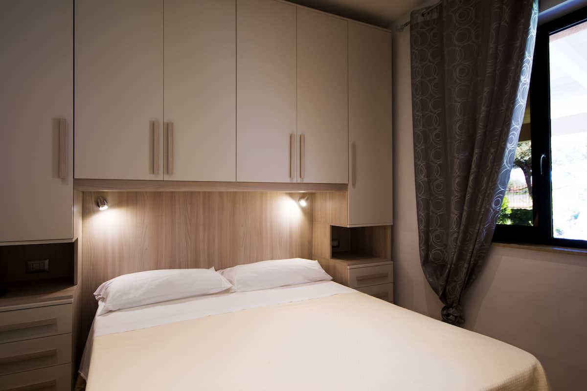 Ein Schlafzimmer mit Bett, Holzkopfseitenverkleidung, Einbauschränken und einem Fenster mit Vorhängen.