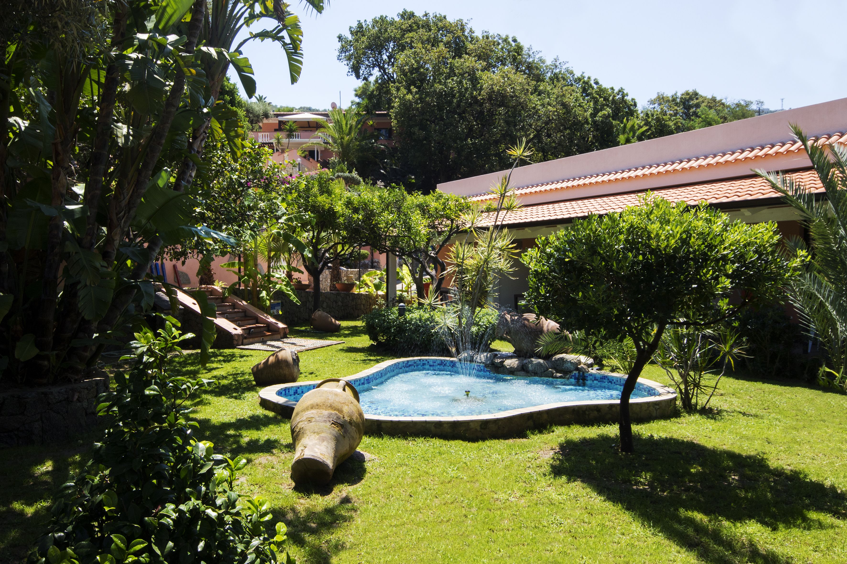 Ein Garten mit einem Swimmingpool, umgeben von üppiger Vegetation und einem Gebäude mit einem Ziegeldach.