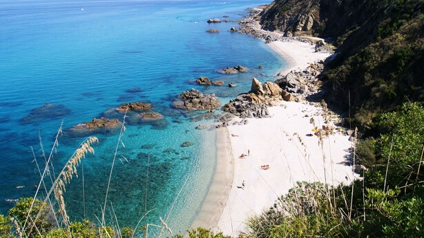 A coastal beach with clear turquoise waters, rocky shoreline, and a sandy beach area. - Park Oasi Residence (Zambrone)