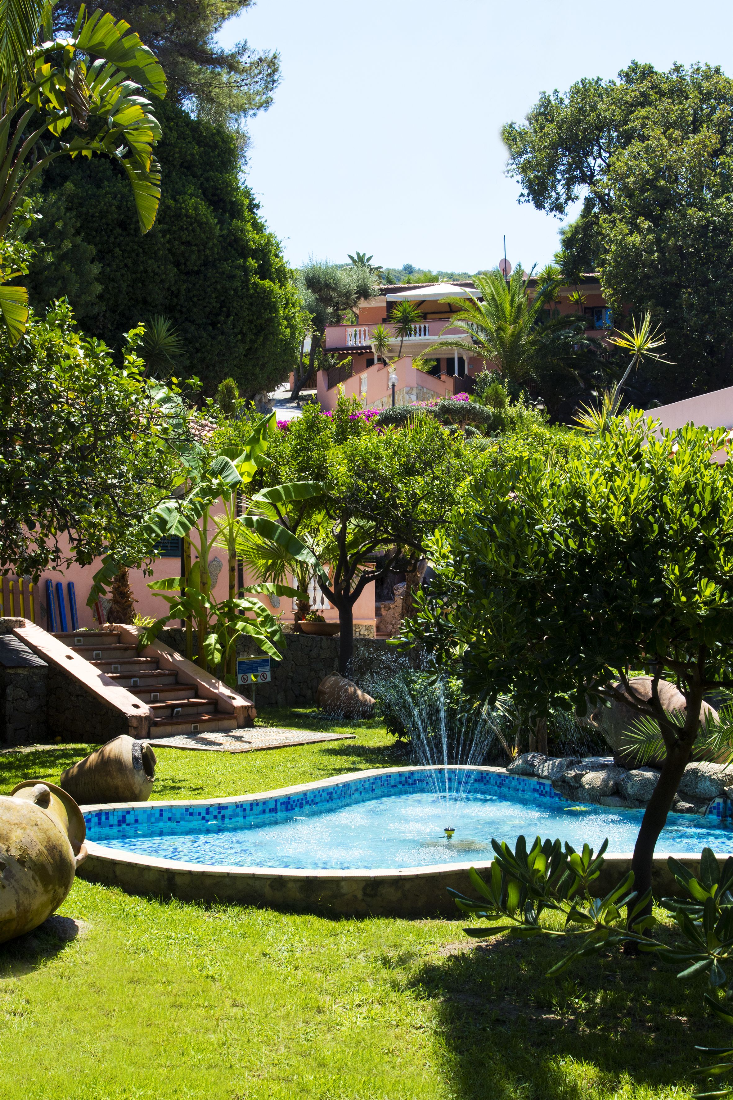 A swimming pool surrounded by lush greenery and a stone staircase leading to a building.