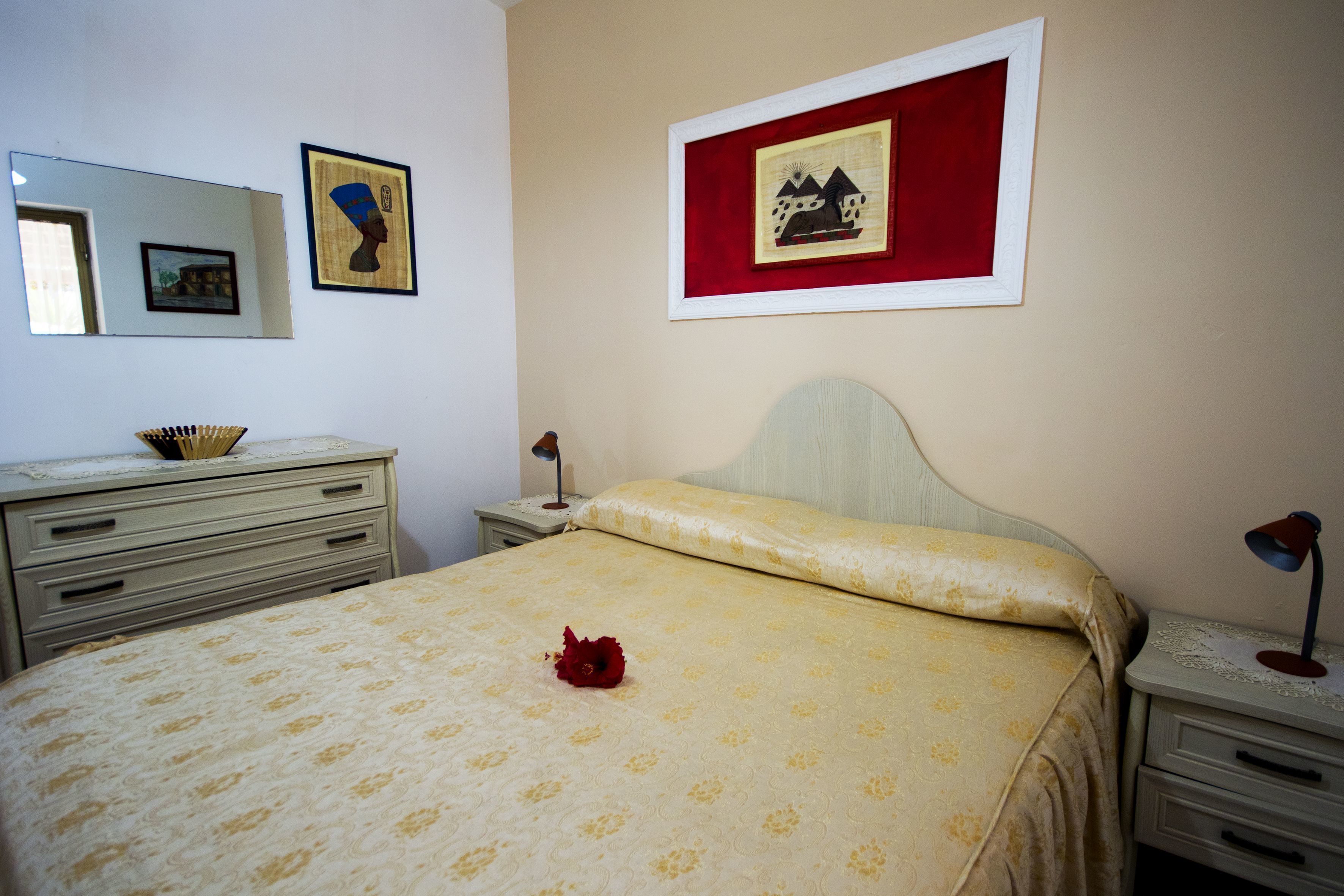 A bedroom with a bed, a nightstand, a dresser, a mirror, and two framed pictures on the wall.