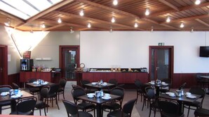Un restaurante con vigas de madera en el techo, varias mesas con sillas, una estación de café y un televisor montado en la pared.