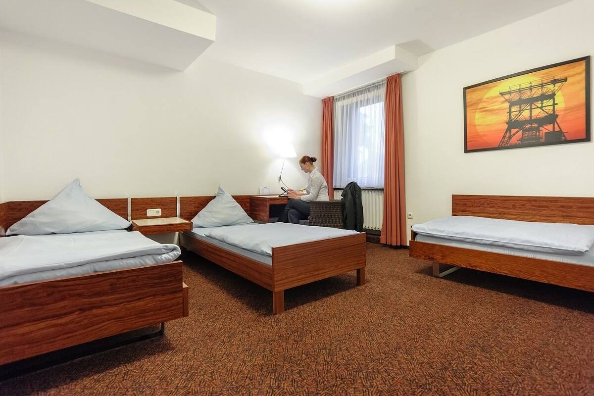 A hotel room with three wooden beds, a desk, and a chair.