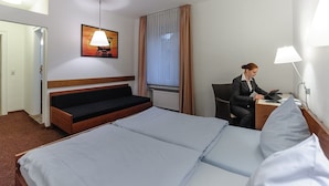 Habitación de hotel con una cama grande, un escritorio con computadora, una silla, una ventana con cortinas y un cuadro en la pared.