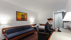 Una habitación de hotel con cama, escritorio con lámpara, sofá y un cuadro colgado en la pared.