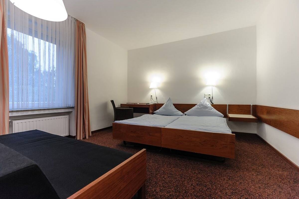 A hotel room with a bed, a desk, a chair, and a window with curtains.