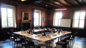 Un salón de conferencias con piso a cuadros, varias mesas dispuestas para reuniones y sillas alrededor de cada una.
