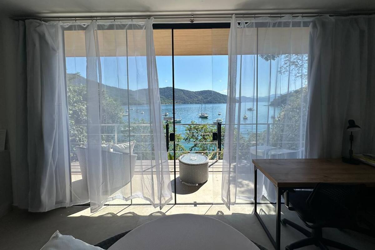 Une pièce dotée d’une grande porte-fenêtre coulissante donnant sur un balcon avec vue sur un lac et des bateaux.