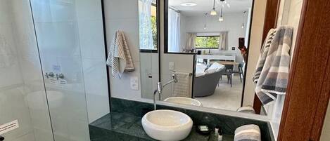 A modern bathroom with a glass shower enclosure, a white sink, and a large mirror with lights above.