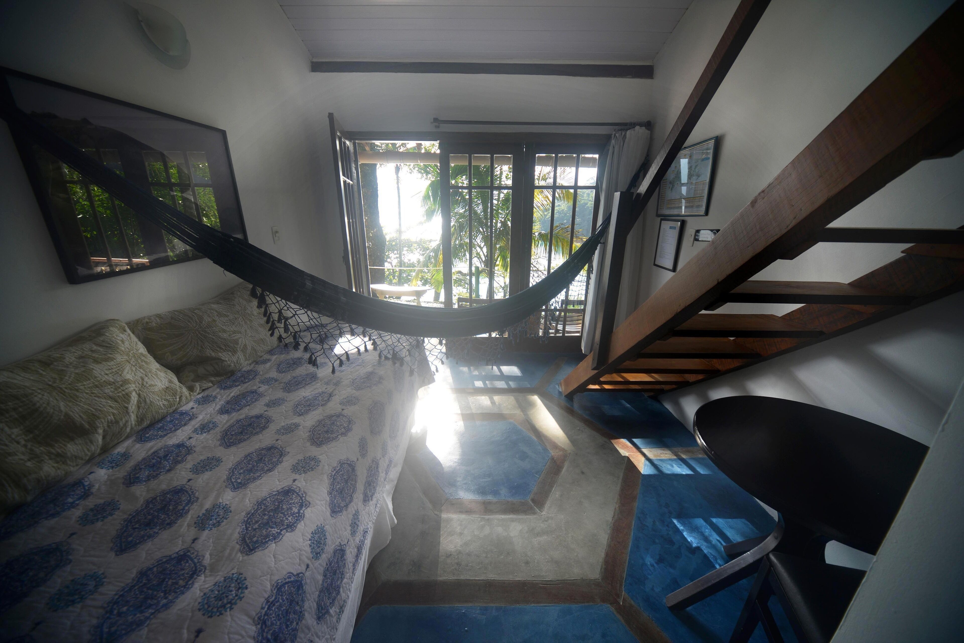 Un dormitorio con cama, una hamaca, una escalera y vistas al exterior.