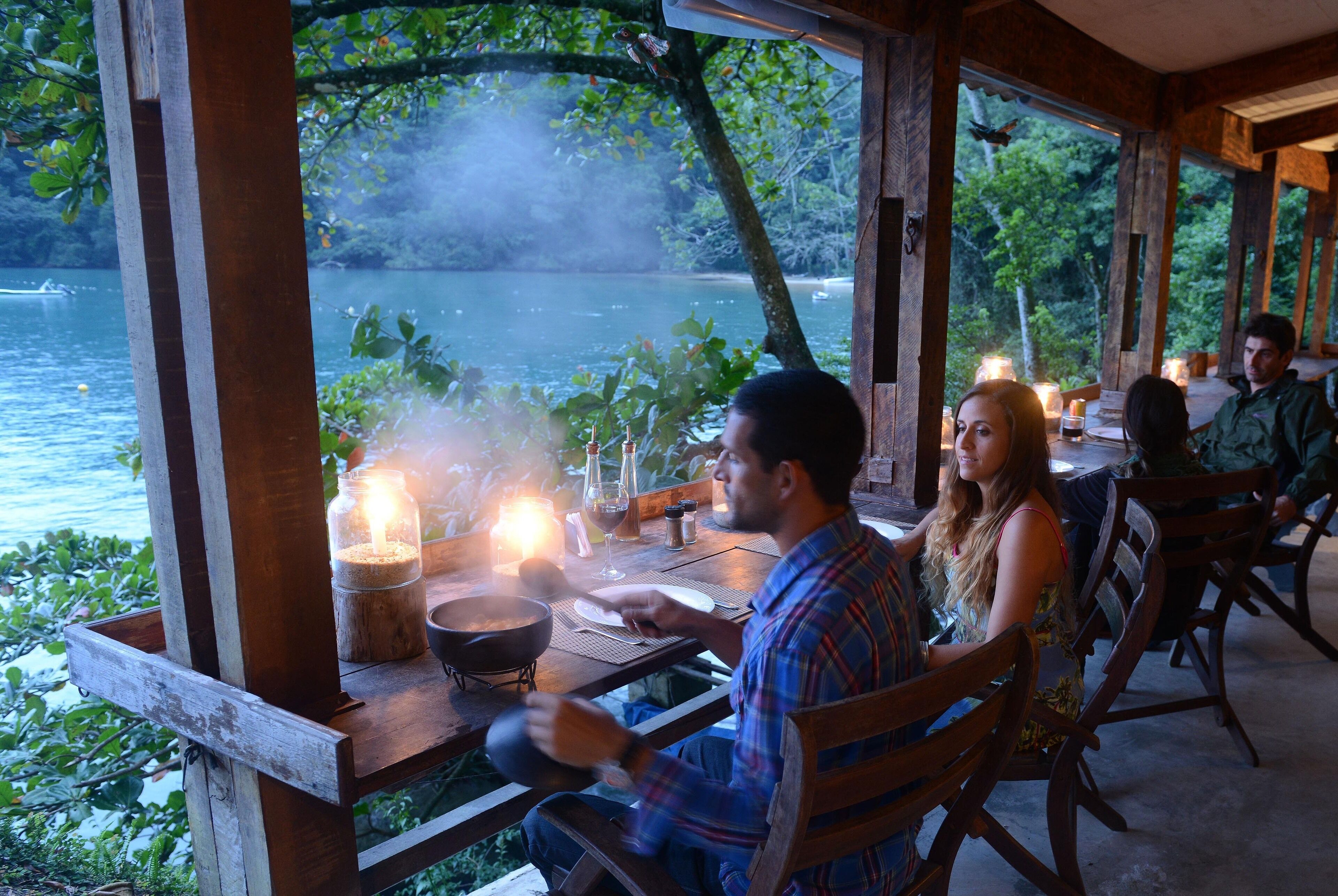 A wooden deck overlooking a lake with a dining table and chairs, a candle, and a pan on the table.