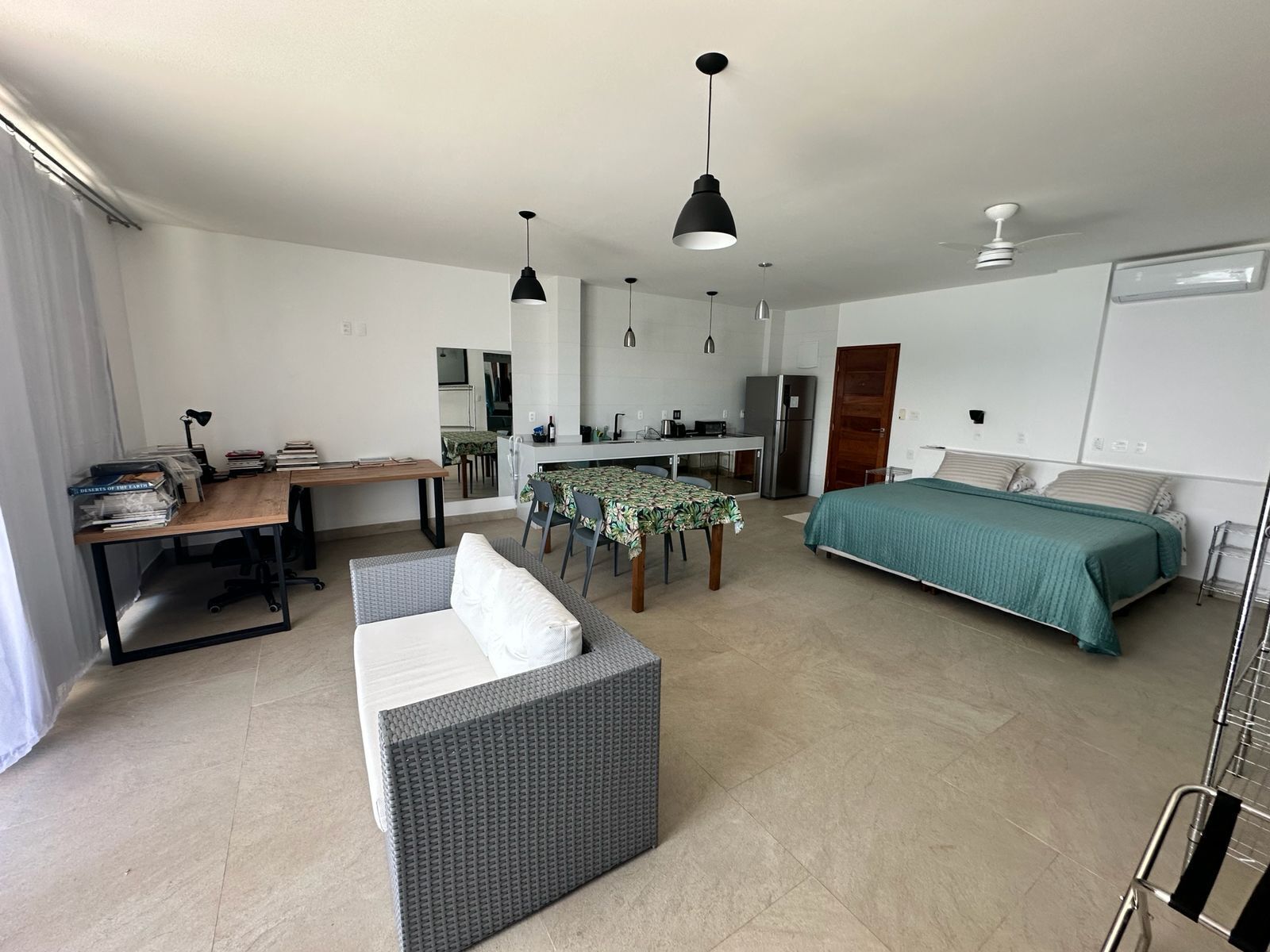 A compact, well-lit room with a dining table, a sofa, a bed, and a kitchenette.