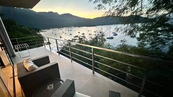 Een balkon met buitenmeubilair, met uitzicht op een meer met boten en bergen op de achtergrond.