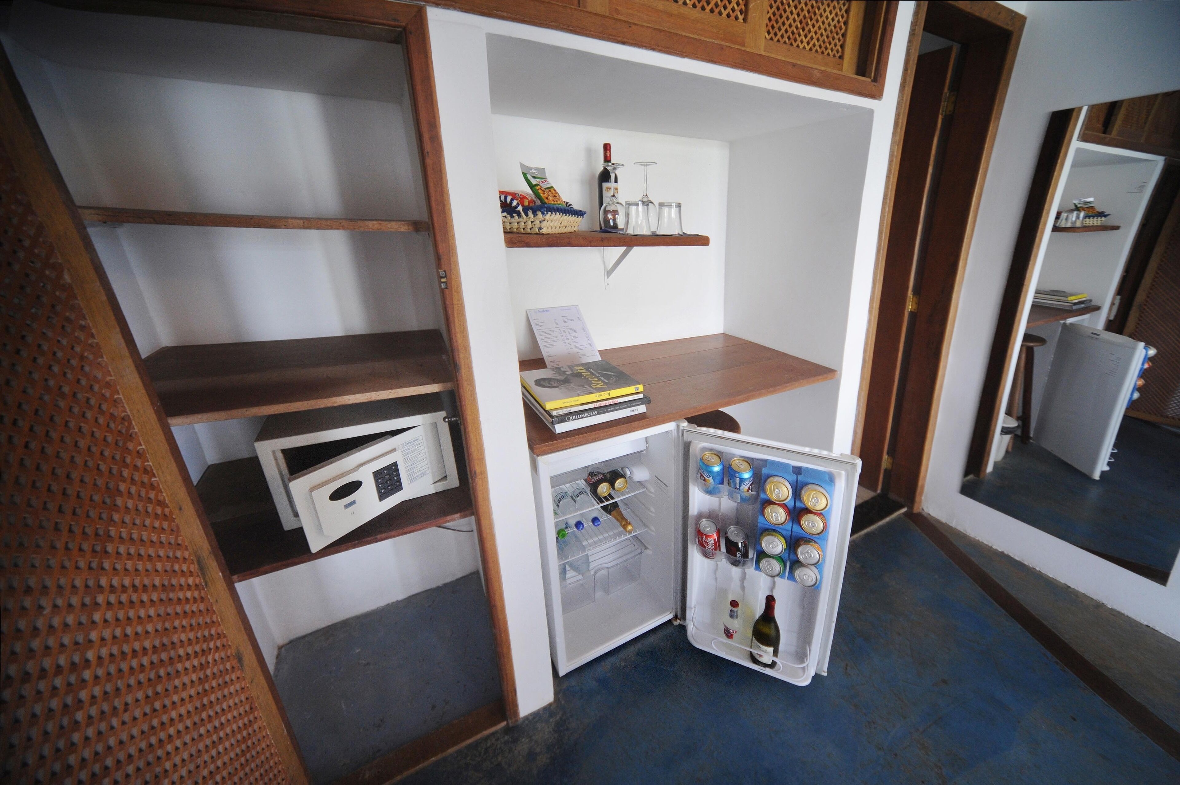 A compact room with a built-in refrigerator, a microwave, and a small shelf with a wine bottle and glasses.