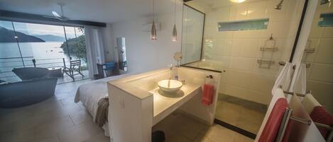 A modern bathroom with a large mirror, a sink, and a shower. There is a view of the sea through large windows.